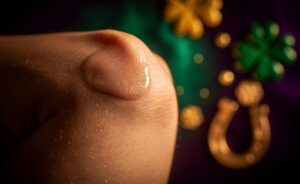 Illustration von einer Hand, die Lipgloss auf einen menschlichen Ellenbogen aufträgt, umgeben von schimmernden Glückssymbolen.