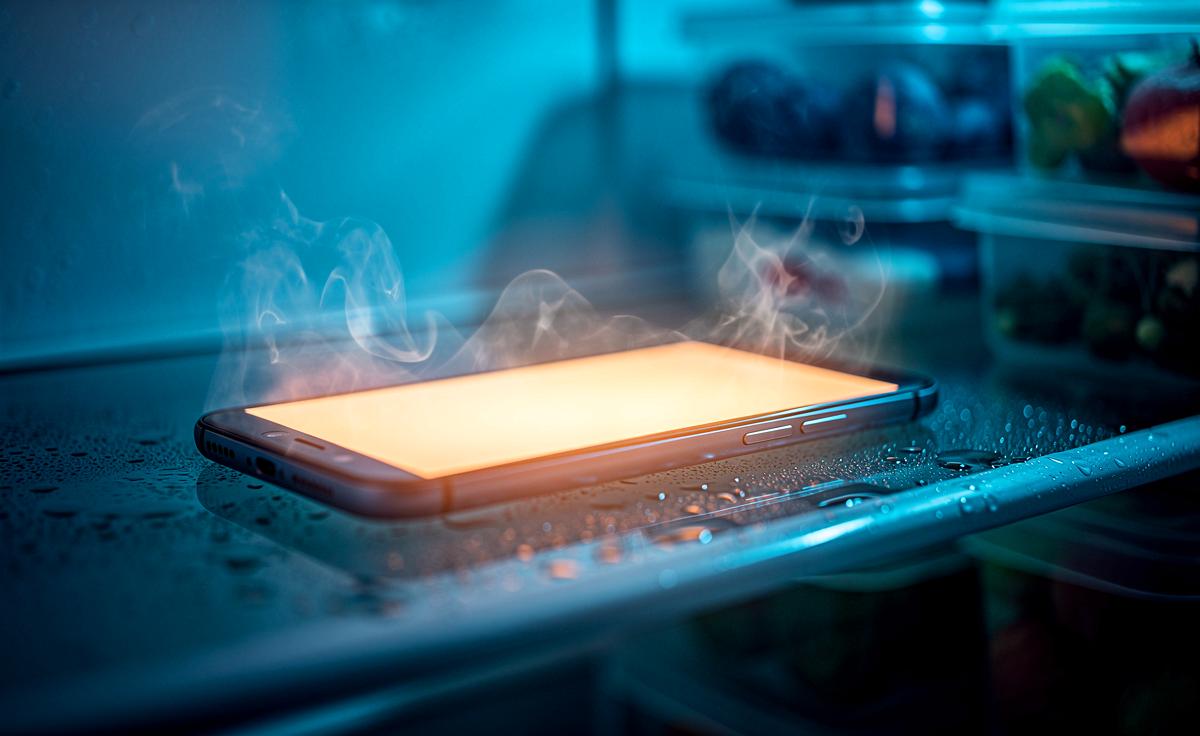 Illustration von einem Smartphone, das in einem geöffneten Kühlschrank zwischen Lebensmitteln liegt, während grafische Strichelemente Wärme und Kälte symbolisieren.